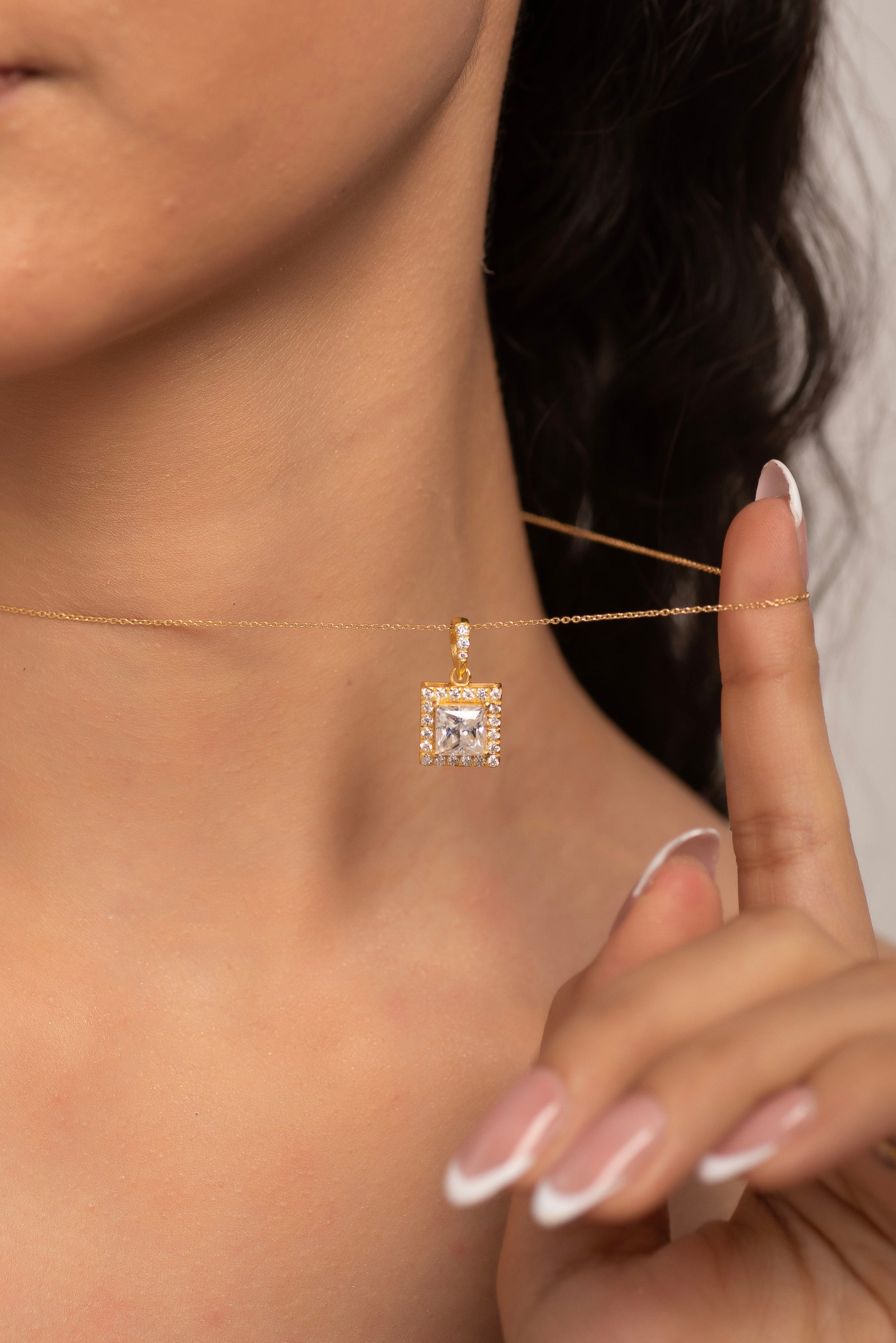 Close-up of a person wearing a gold necklace with a princess cut diamond pendant.