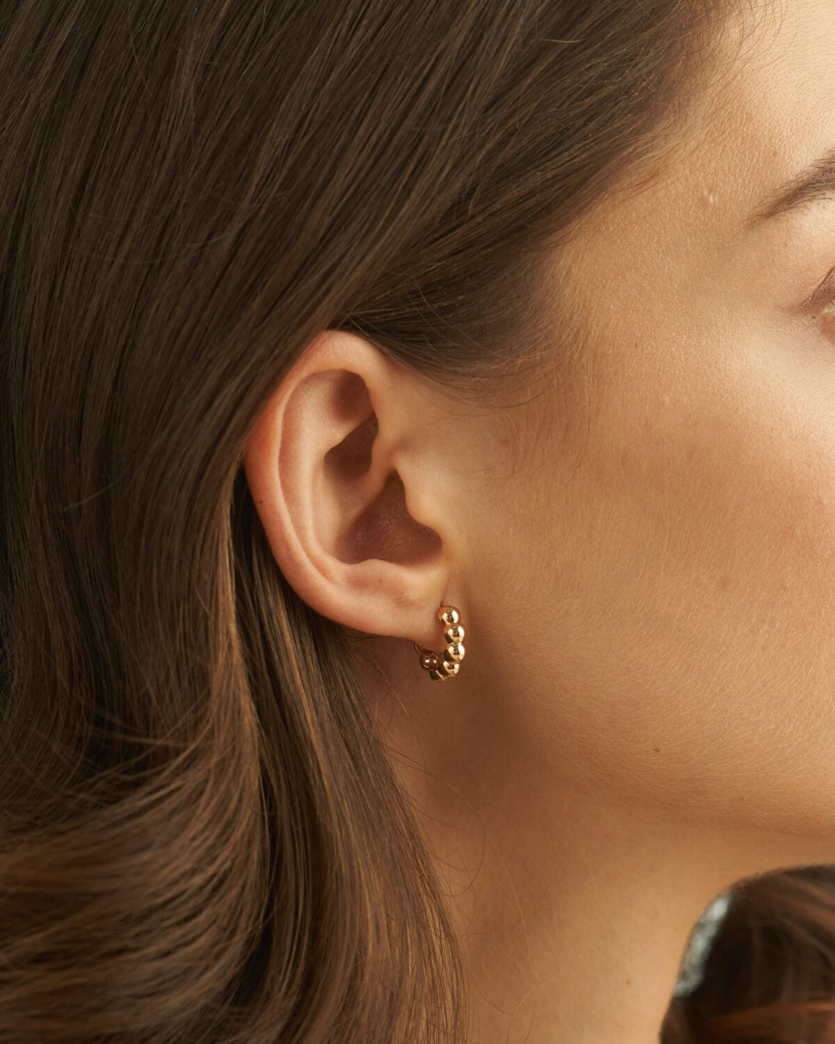 Bold bubble bead hoop earrings worn by a model with hair tucked behind the ear.