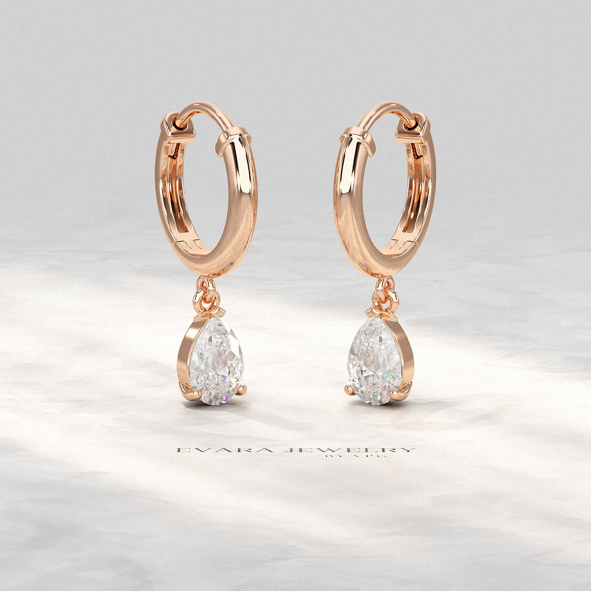 1 carat pear cut diamond hoops displayed on a white marble background